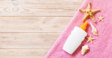 Beach flat lay accessories with copy space. Pink towel, starfish and a bottle of sunblock on banner wooden background. Summer holiday concept