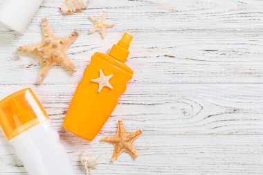 Beyaz ahşap masa üzerinde deniz kabukları ile güneş kremi şişeleri. Seyahat h