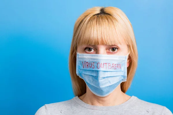 Portretul femeii purtând mască medicală cu text focar de virus pe fundal albastru. Conceptul de coronavirus. Protecție respiratorie — Fotografie, imagine de stoc