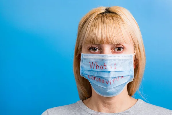 Porträtt av en kvinna som bär medicinsk mask med vad som är coronavirus ord på blå bakgrund. Coronavirus och hälsovårdskoncept — Stockfoto