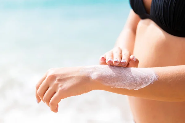 Pretty girl is putting sun lotion on her hand at the beach — Stock Photo, Image