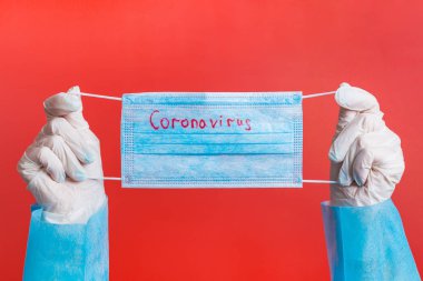 Tıbbi eldivenli kadın eller kırmızı arka planda üzerinde koronavirüs yazılı koruyucu maske tutuyor. Sağlık hizmeti konsepti. Coronavirus konsepti