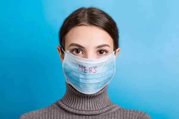 Portretul unei tinere care poartă mască medicală cu cuvântul MERS pe fundal albastru. Protejați-vă sănătatea. Conceptul Coronavirus — Fotografie, imagine de stoc