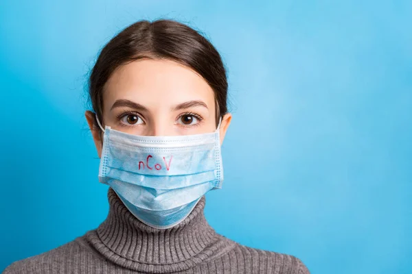 Portrait of a woman wearing medical mask with nCoV word at blue background. Coronavirus and healthcare concept — Stockfoto