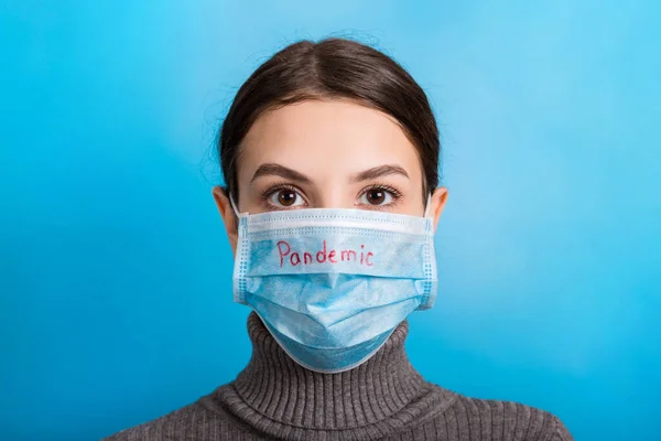 Potret seorang wanita yang mengenakan topeng medis dengan kata pandemi dengan latar belakang biru. Konsep Coronavirus dan layanan kesehatan — Stok Foto