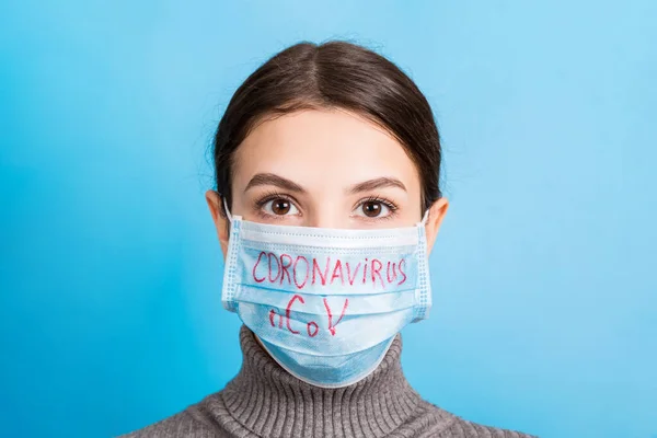 Portrait of young woman wearing medical mask with coronavirus nCoV word at blue background. Protect your health. Coronavirus concept — Stok fotoğraf