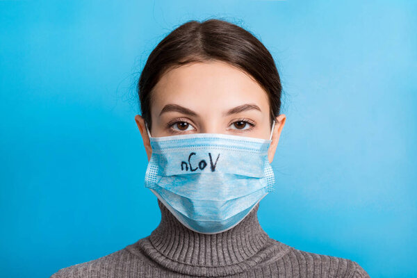 Portrait of young woman wearing medical mask with nCoV word at blue background. Protect your health. Coronavirus concept