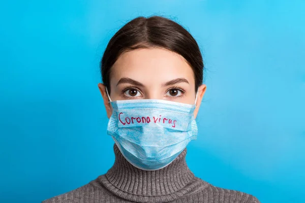 Portrait of pretty woman wearing medical mask with coronavirus text at blue background. Coronavirus concept. Respiratory protection — Stockfoto
