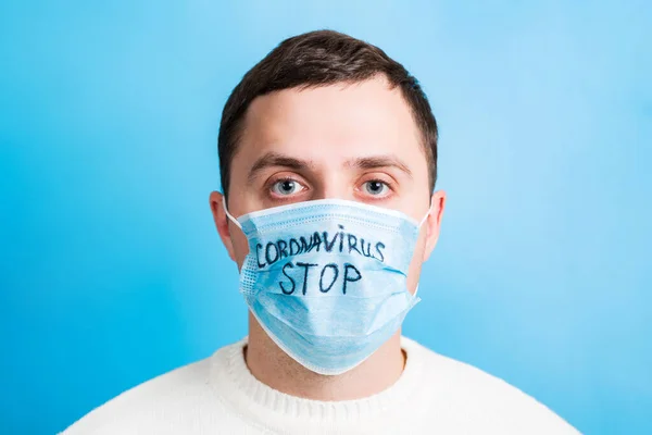 Portrait of young sick man in medical mask with stop coronavirus word at blue background. Respiratory protection. Coronavirus concept — Stockfoto
