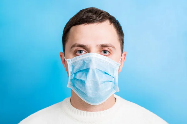 Portrait of young man wearing medical mask at blue background. Coronavirus concept. Respiratory protection — Stockfoto