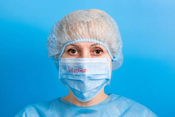 Portret van een vrouw in medisch uniform en masker met infectietekst op blauwe achtergrond. Bescherm je gezondheid. Coronavirusconcept — Stockfoto
