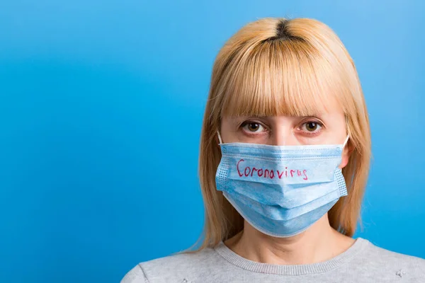 Portretul unei femei în mască medicală cu text coronavirus pe fundal albastru. Conceptul de coronavirus. Protecție respiratorie — Fotografie, imagine de stoc
