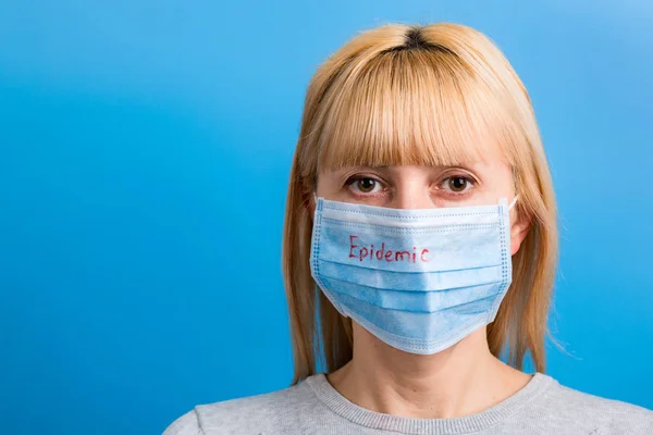 Portretul femeii purtând mască medicală cu cuvânt epidemic pe fundal albastru. Protejați-vă sănătatea. Conceptul Coronavirus — Fotografie, imagine de stoc