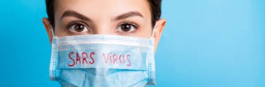 Mavi arka planda Sars virüsü olan tıbbi maskeli bir kadının portresi. Coronavirus konsepti. Solunum koruması.
