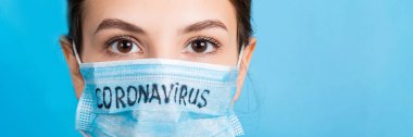 Mavi arka planda Coronavirus metni olan tıbbi maskeli bir kadının portresi. Coronavirus konsepti. Solunum koruması.