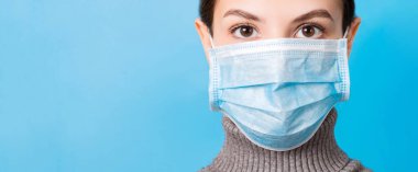 Mavi arka planda tıbbi maske takan genç bir kadının portresi. Sağlığınızı koruyun. Coronavirus konsepti.