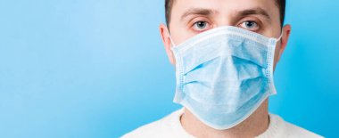 Portrait of young man wearing medical mask at blue background. Coronavirus concept. Respiratory protection.