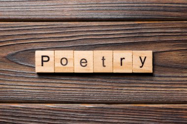 Tahta blokta yazılmış bir şiir kelimesi. Şiir metni ahşap masa üzerinde, üstteki görünüm konseptiniz için..