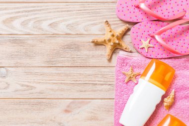 Beach düz döşeme aksesuarları üst görünümü. deniz kabukları, denizyıldızı, havlu ve kopya alanı ile ahşap tahta arka plan üzerinde flip-flop ile güneş kremi şişe.