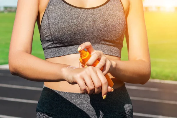 Crop image of a woman protecting her hands and arms with sunblock before training at the stadium on a sunny day. Skincare concept.