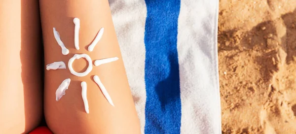 Sun cream is drawn in sun shape on tanned woman\'s leg who is relaxing on the towel at the beach. Cancer care concept.