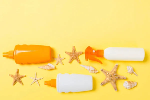 sunscreen cream with starfish and seashells in bottles on yellow background, top view.