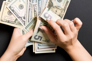 İş kadınının elleri renkli arka planda beş dolar ve diğer dolar banknotları sayar. Maaş ve ücret kavramı. Yatırım kavramına en üst düzey bakış.