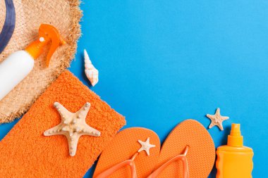 Summer beach flat lay accessories. Sunscreen bottle cream, straw hat, flip flops, towel and seashells on colored Background. Travel holiday concept with copy space.