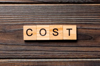 Tahta blokta yazılmış bir kelime. En iyi görünüm konseptiniz için tahta masadaki maliyet metni.