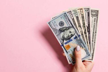 Renkli arka planda para fan tutarak kadın el üst görünümü. Çeşitli dolar banknotları. Kopya alanı ile kredi ve borç kavramı.