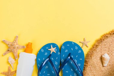parmak arası terlik, hasır şapka, denizyıldızı, güneş kremi şişesi, sarı arka plan üst görünümünde vücut losyon sprey . düz yatıyordu yaz plaj deniz aksesuarları arka plan, tatil konsepti.