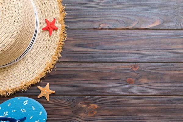 Hasır şapka, mavi parmak arası terlik ve denizyıldızı koyu ahşap bir arka plan üzerinde. kopya alanı ile üst görünüm yaz tatili konsepti.
