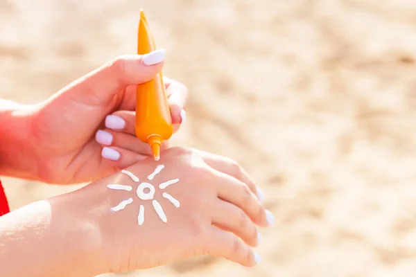 Young woman is applying sun cream on her hand in sun shape at the beach.