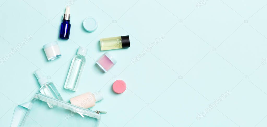Group of small bottles for travelling on blue background. Copy space for your ideas. Flat lay composition of cosmetic products. Top view of cream containers with cotton pads.