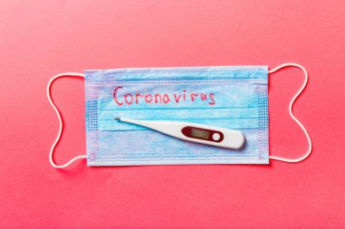 Koruyucu tıbbi maskenin üst görüntüsü ve kırmızı arka planda bir termometre. Coronavirus kelimesi. Ncov ve covid salgını. Salgın hastalık konsepti. Sağlığınızı koruyun..