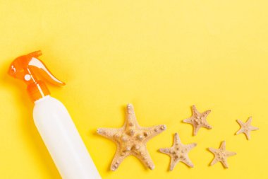 Sarı ahşap masa üzerinde deniz kabukları ile güneş kremi şişeleri.