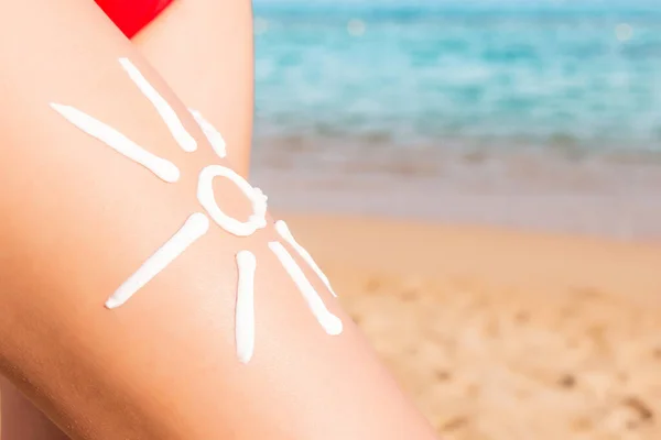 太阳形状由海洋背景中女性腿上的防晒霜制成 — 图库照片