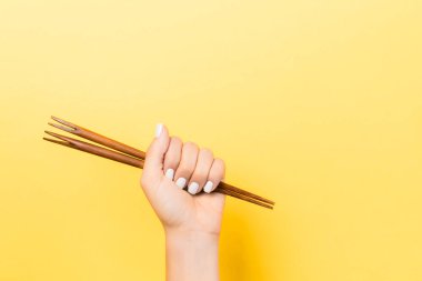 Sarı arka plan üzerinde yumruk çubukları tutan kadın el Kırpılmış görüntü. Kopyalama alanı ile Asya gıda kavramı.