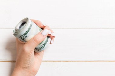 Kadın eli sıkıca sarılmış bir tomar parayı tutuyor. Ahşap arka planda 100 doların en üst görüntüsü. Kopya alanı ile yatırım kavramı.