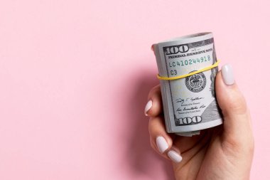 Renkli arka plan üzerinde haddelenmiş para bir paket tutan kadın el üst görünümü. Yüz dolar. Tasarım için boş alan ile Iş konsepti. Sadaka ve ipuçları kavramı.