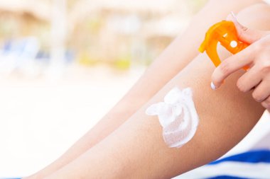 Kız şezlong üzerinde oturuyor ve plajda güneş kremi oh bacak uyguluyor.