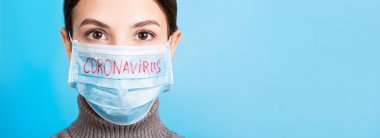 Mavi arka planda Coronavirus NCoV ile tıbbi maske takan genç bir kadının portresi. Sağlığınızı koruyun. Coronavirus konsept pankartı.
