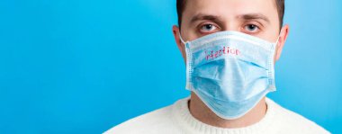 Mavi arka planda enfeksiyon mesajlı tıbbi maske takan hasta bir adamın portresi. Coronavirus konsepti. Sağlık afişinizi koruyun..