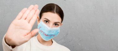 Coronavirus metniyle tıbbi maskeli bir kadının portresi ve gri çimento arka planında dur işareti. Coronavirus konsepti. Solunum koruması.