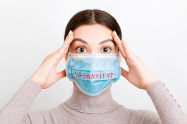 Beyaz arka planda Coronavirus yazılı tıbbi maske takan oldukça şok olmuş bir kadının portresi. Coronavirus konsepti. Solunum koruması.