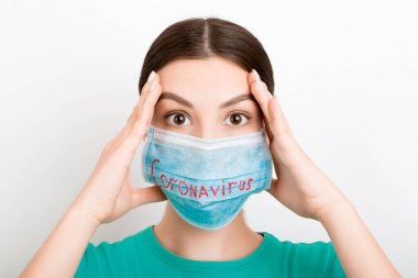 Beyaz arka planda Coronavirus yazılı tıbbi maske takan oldukça şok olmuş bir kadının portresi. Coronavirus konsepti. Solunum koruması.
