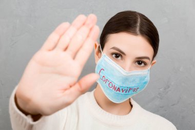 Coronavirus metniyle tıbbi maskeli bir kadının portresi ve gri çimento arka planında dur işareti. Coronavirus konsepti. Solunum koruması.