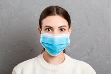 Gri çimento arka planda tıbbi maske takan genç bir kadının portresi. Sağlığınızı koruyun. Coronavirus konsepti.
