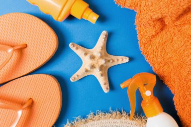 Summer beach flat lay accessories. Sunscreen bottle cream, straw hat, flip flops, towel and seashells on colored Background. Travel holiday concept with copy space.