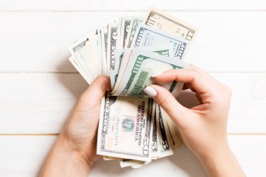 İş kadınının elleri tahtadan arka planda yüz dolarlık banknotları sayıyor. Maaş ve maaş kavramı. Yatırım konseptinin en üst görünümü.
